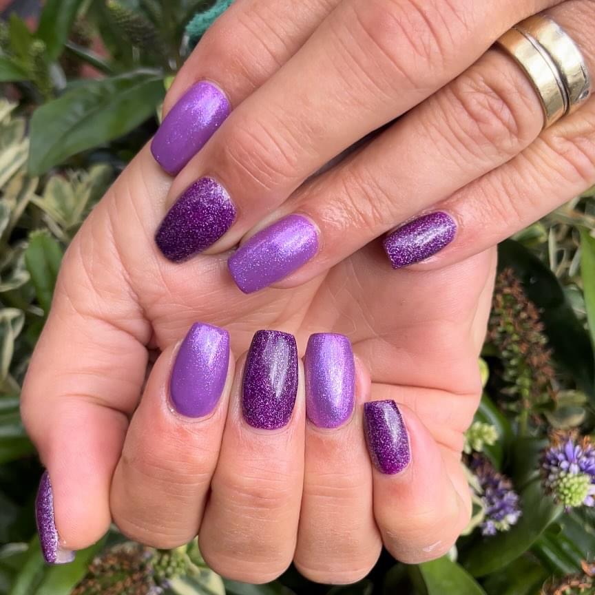 Paarse shimmer- en glitternagels tegen groen blad